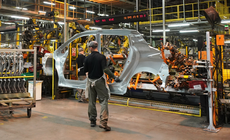 Factory workers assembling a car body using robotic arms.