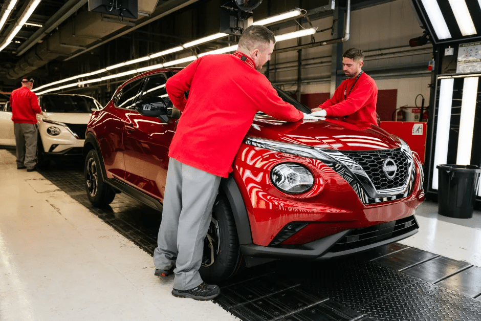Workers inspecting a red Nissan Juke on an assembly line.