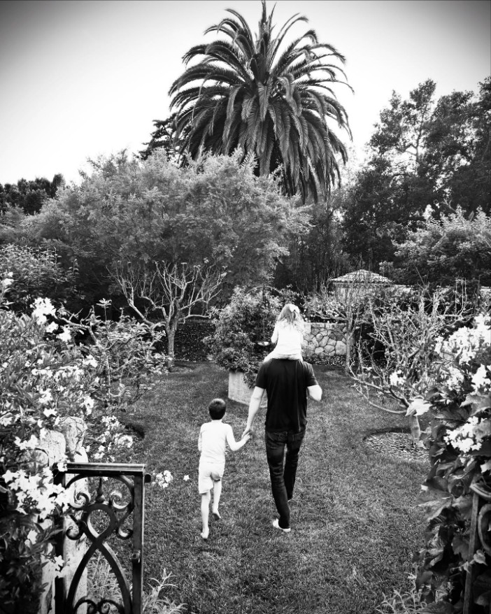 Black and white photo of a man walking with two young children in a garden.