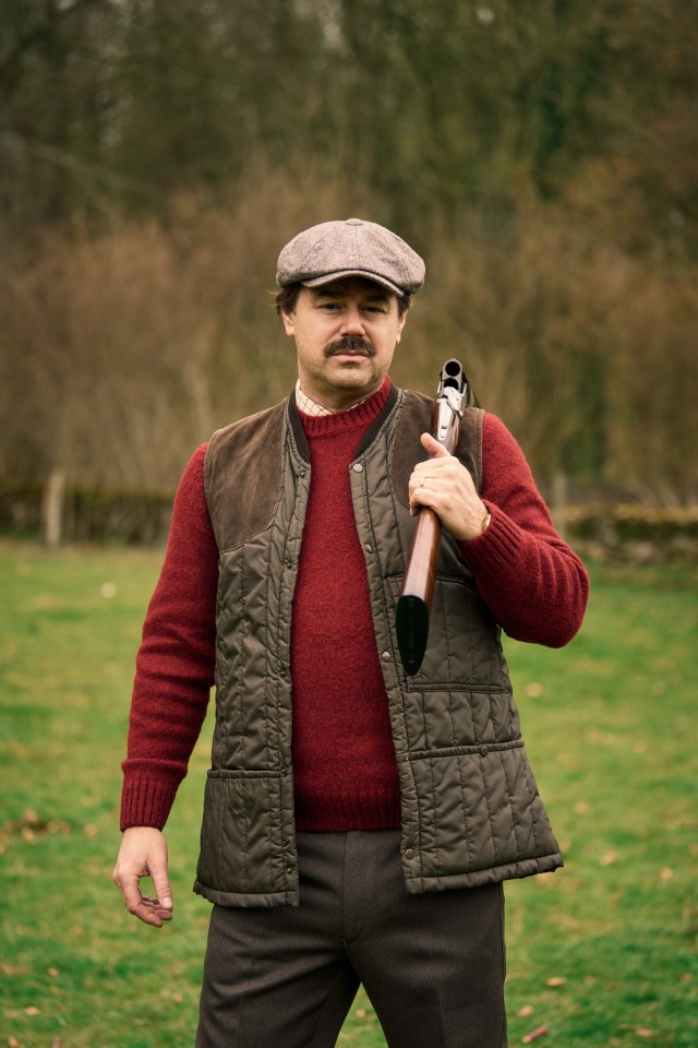 Man in tweed cap and hunting vest carrying a shotgun.