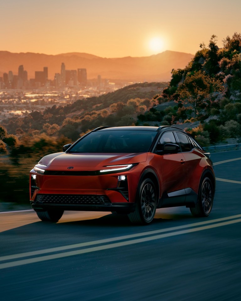 Red Toyota C-HR BEV driving on a road at sunset.
