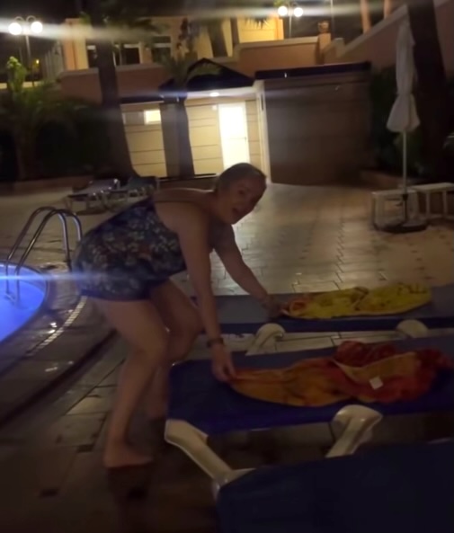 Woman removing towels from sunbeds at night.